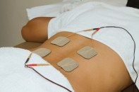 Patient applying electrical stimulation therapy ( TENS ) on his back